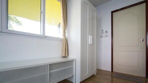 A hallway with a white bench, a door, and a window with curtains. - Pranee Guesthouse (Koh Tao)