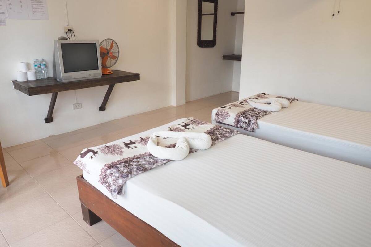 A hotel room with two beds, a TV on a wooden shelf, a fan, and a mirror on the wall.