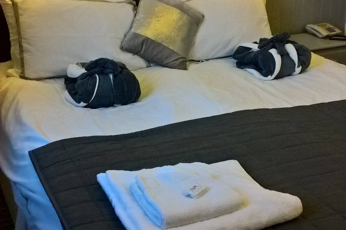 Uma cama bem arrumada com almofadas, uma toalha dobrada e um quadro na parede.