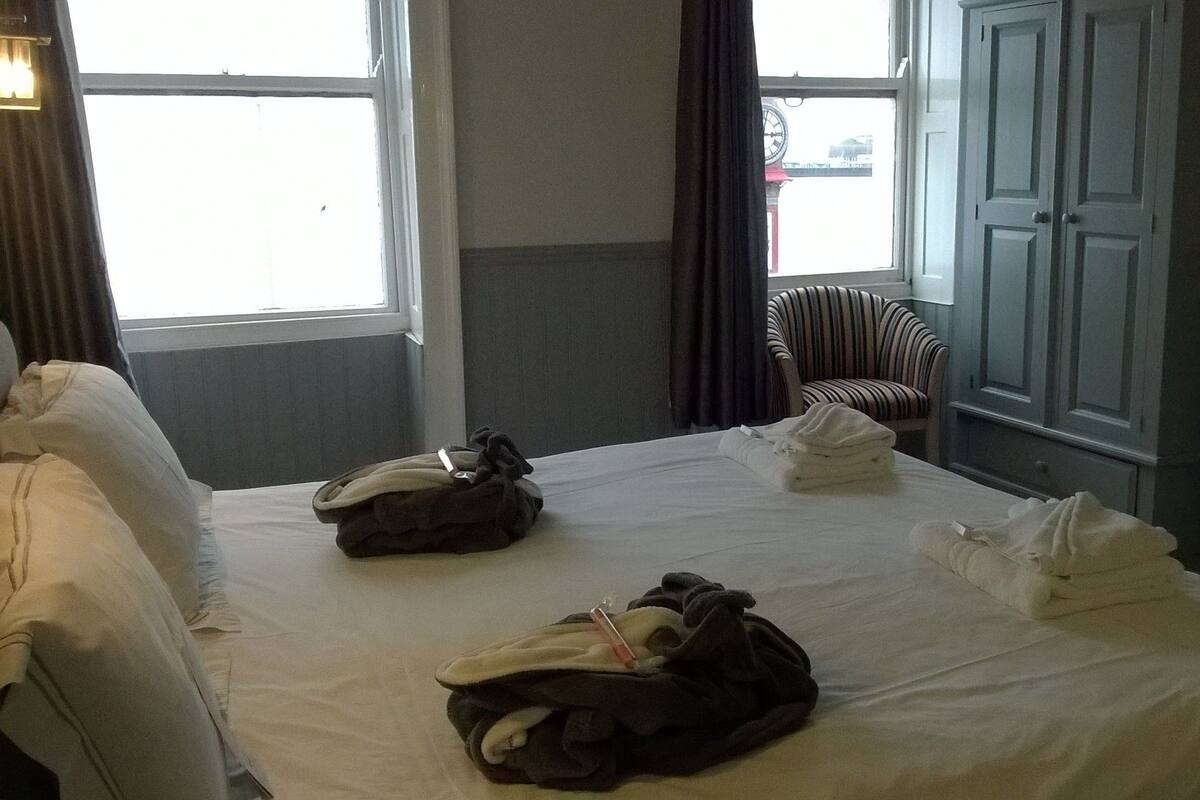 Quarto de hotel com duas camas, uma cadeira, cômoda e janela com vista para um edifício.