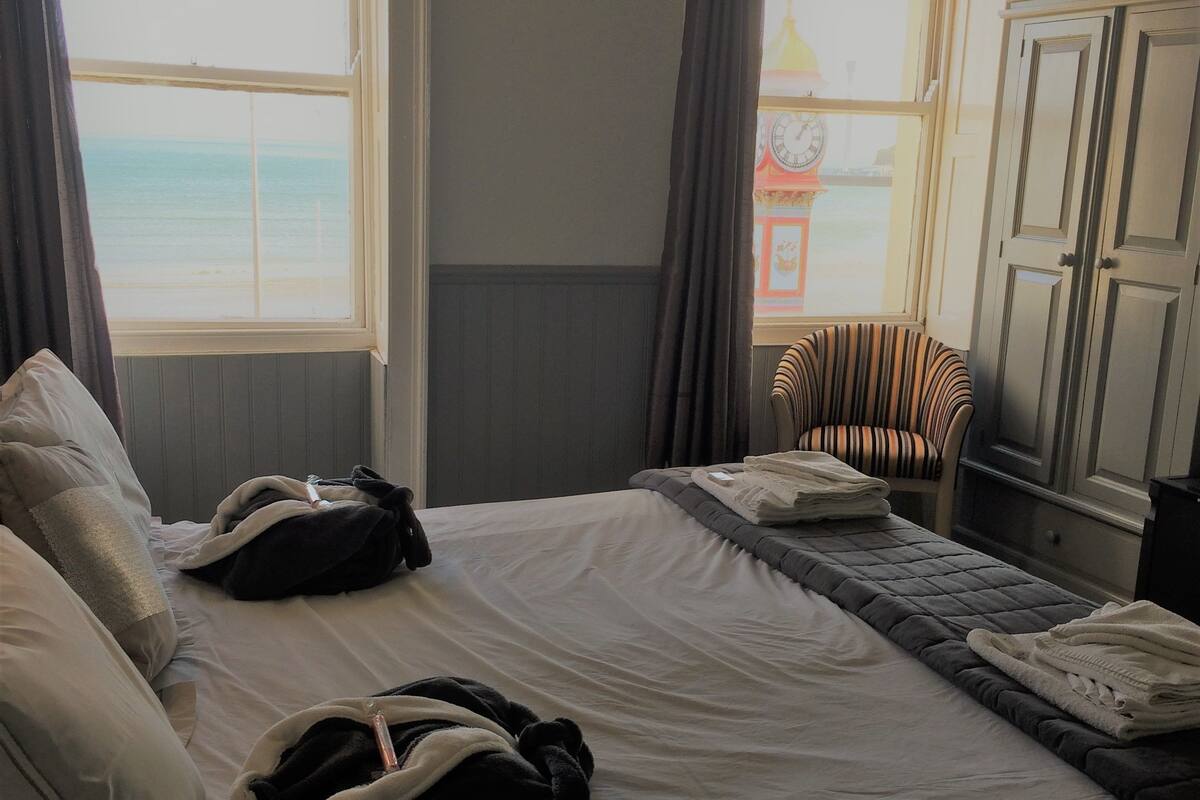 Quarto de hotel com uma cama, uma cadeira e vista para o mar.