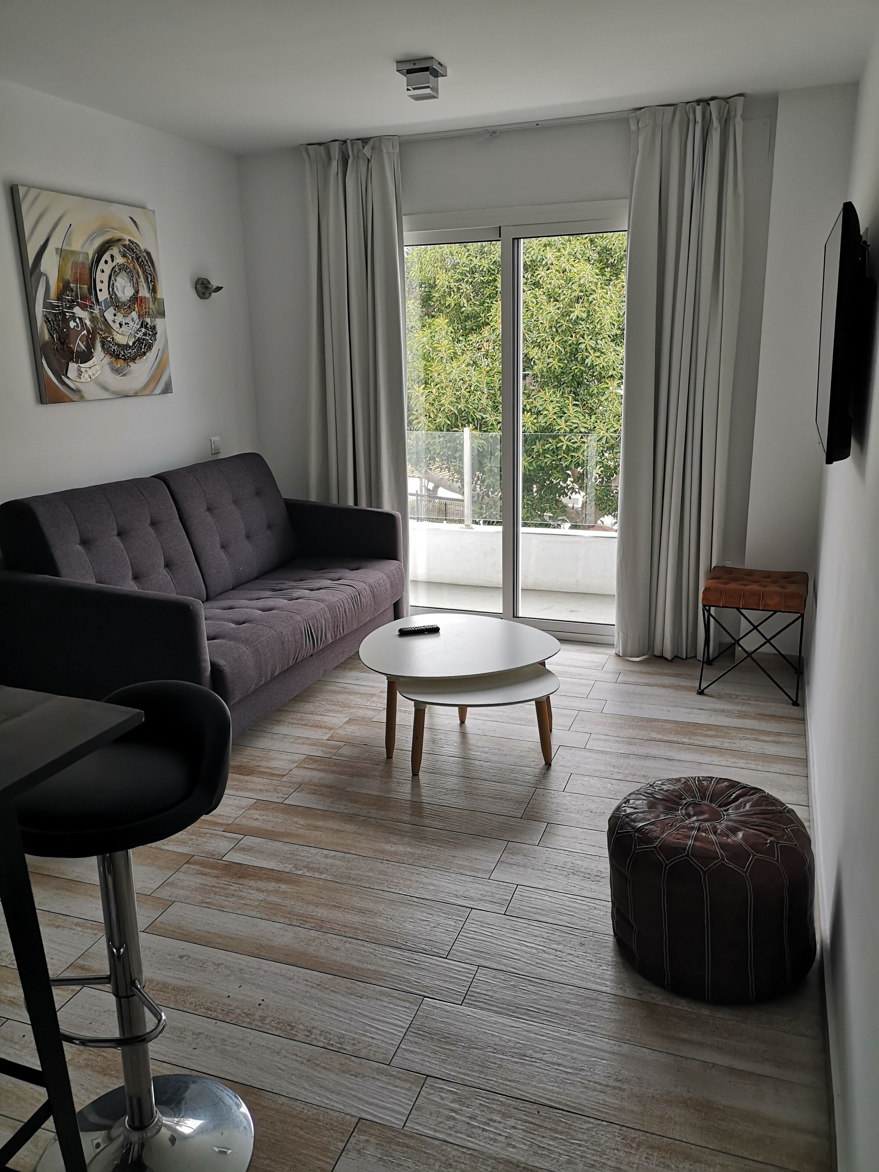 Una sala moderna con un sofá gris, una mesa de centro redonda, un taburete negro y un reposapiés marrón.