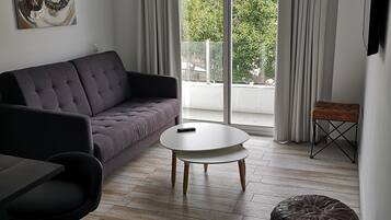 Una sala moderna con un sofá gris, una mesa de centro redonda, un taburete negro y un reposapiés marrón.
