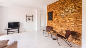 Ein modernes Wohnzimmer mit einer Holzwand, einem Flachbildfernseher, zwei Stühlen und einem kleinen Tisch mit Früchten.