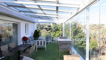 Une terrasse extérieure moderne dotée d’un toit en verre, d’un gazon synthétique vert et d’un aménagement avec des sièges.