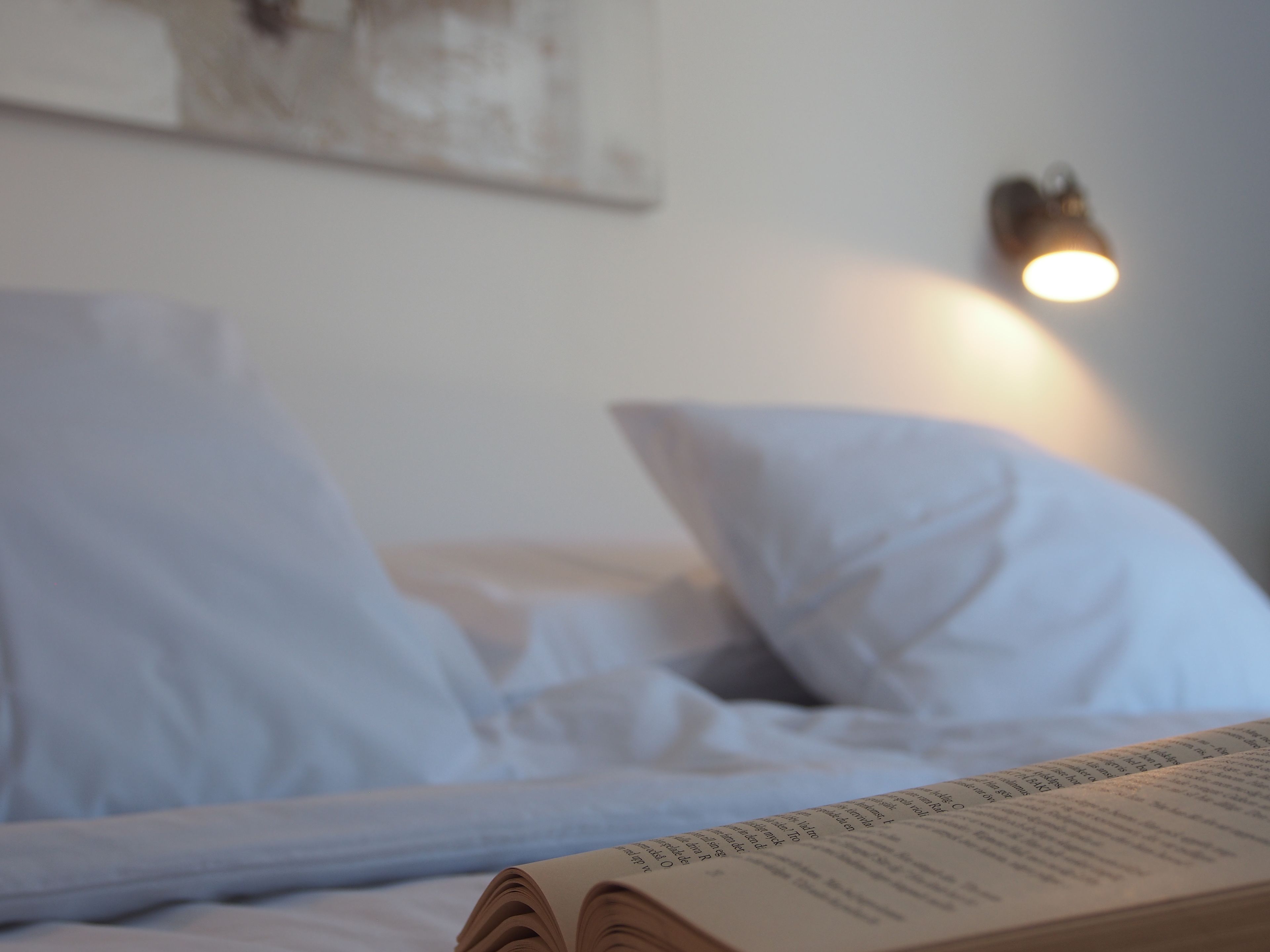 Een bed met witte lakens en een open boek erop.