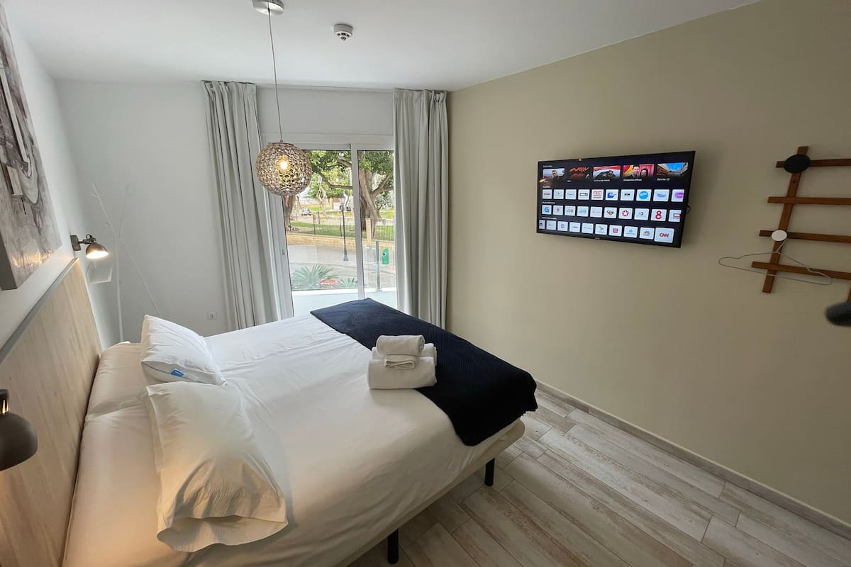 A hotel room with a bed, a TV mounted on the wall, and a window with curtains.