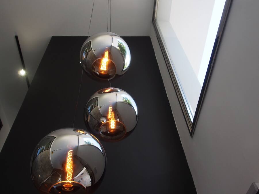 Trois suspensions sphériques, dont les ampoules à filament apparent sont suspendues à un plafond noir.