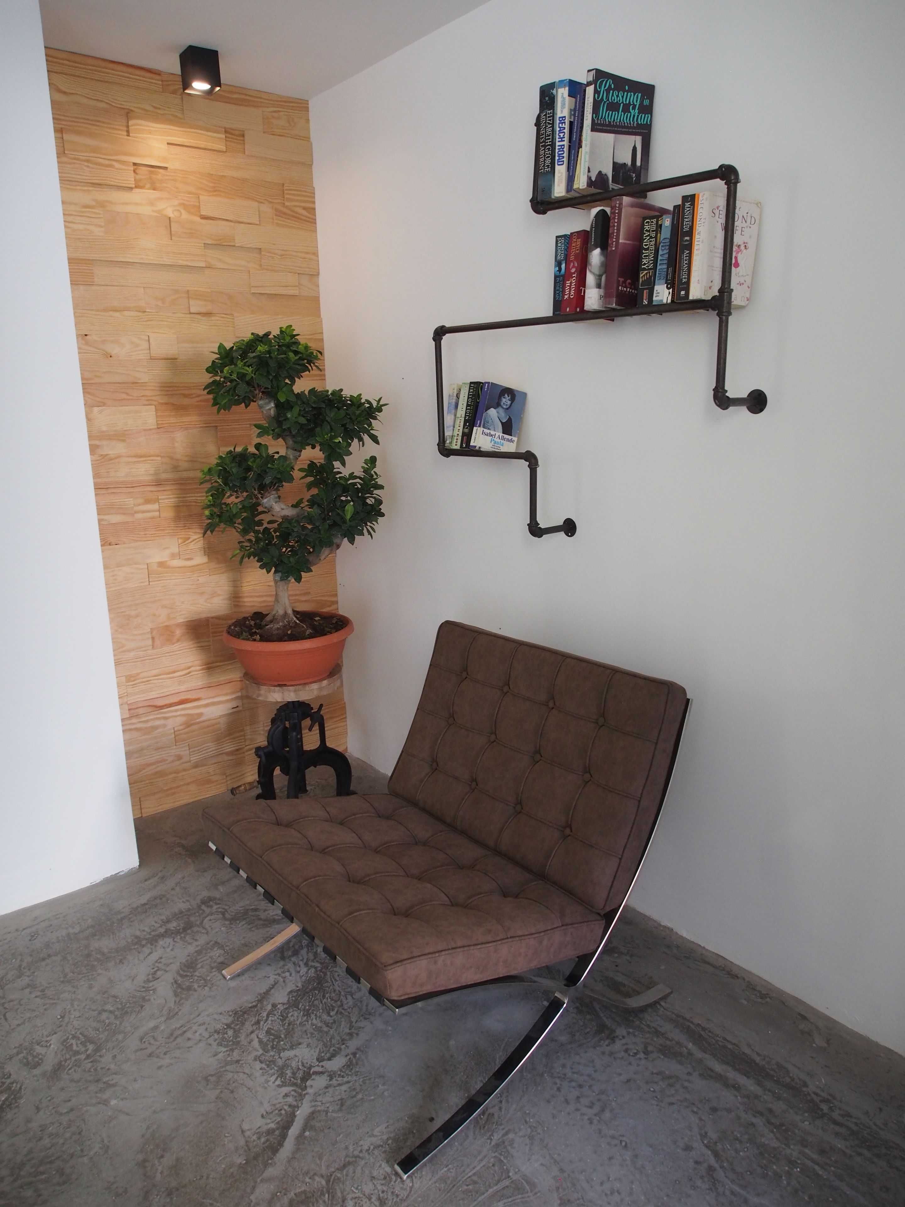 Una habitación de esquina con un banco acolchado marrón, una planta en maceta, un revestimiento de madera y estanterías llenas de libros.