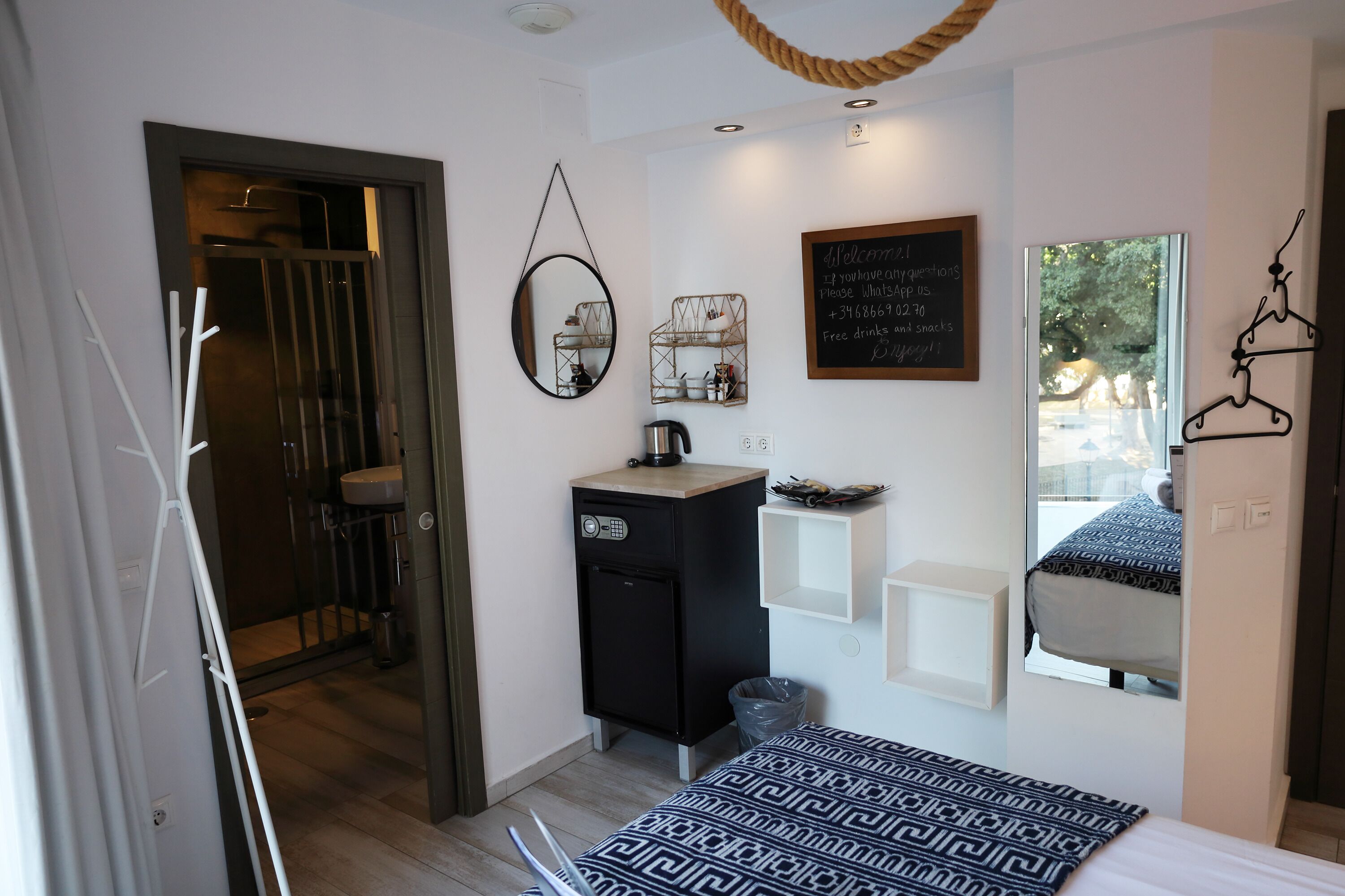 Habitación de hotel moderna con una cama, un escritorio pequeño, un espejo, una lámpara colgante y una ventana con vistas.