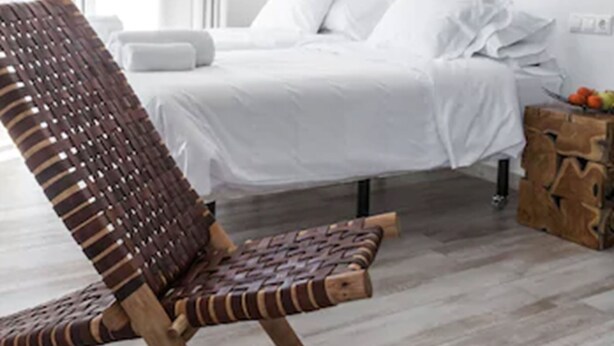 Ein modernes Schlafzimmer mit einem großen Bett, einem gewobenen Sessel und einem einzigartigen Wandkunstwerk.