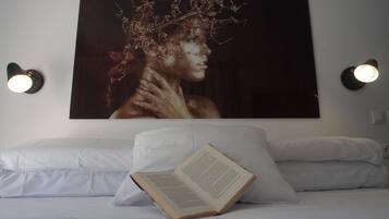 A bedroom with a large framed artwork on the wall, a bedside table with a book, and two wall-mounted lamps.