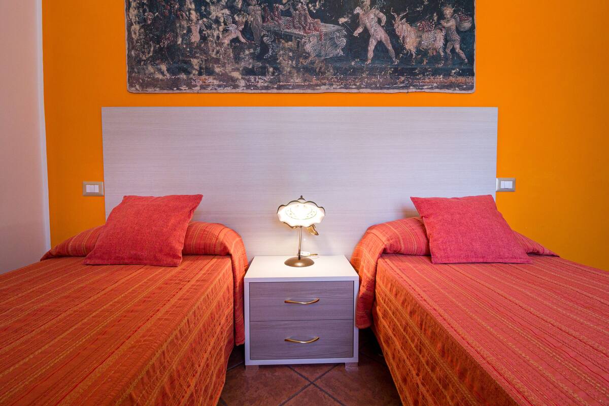 A room with two beds, a nightstand with a lamp, and a painting on the wall.