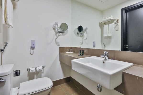 A bathroom with a white sink, a mirror, a toilet, and a hairdryer mounted on the wall. - Wyndham Garden Ribeirao Preto Convention (Ribeirão Preto)