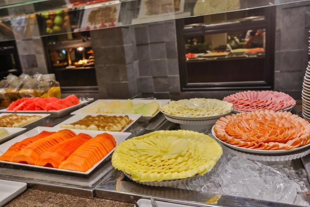 A buffet with various food items including sliced meats, fruits, and desserts.