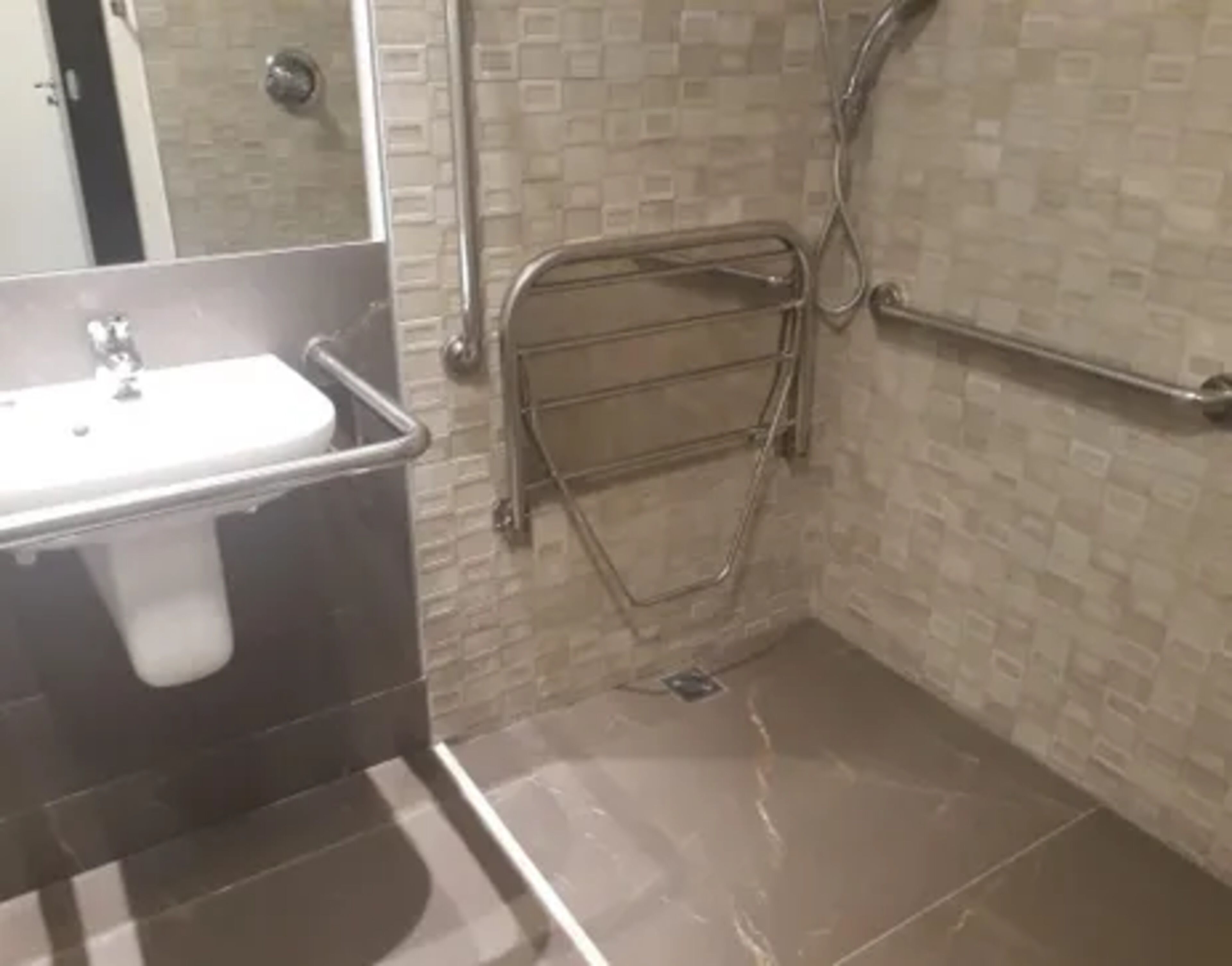 Un baño con lavamanos, espejo y zona de ducha con barra de apoyo.