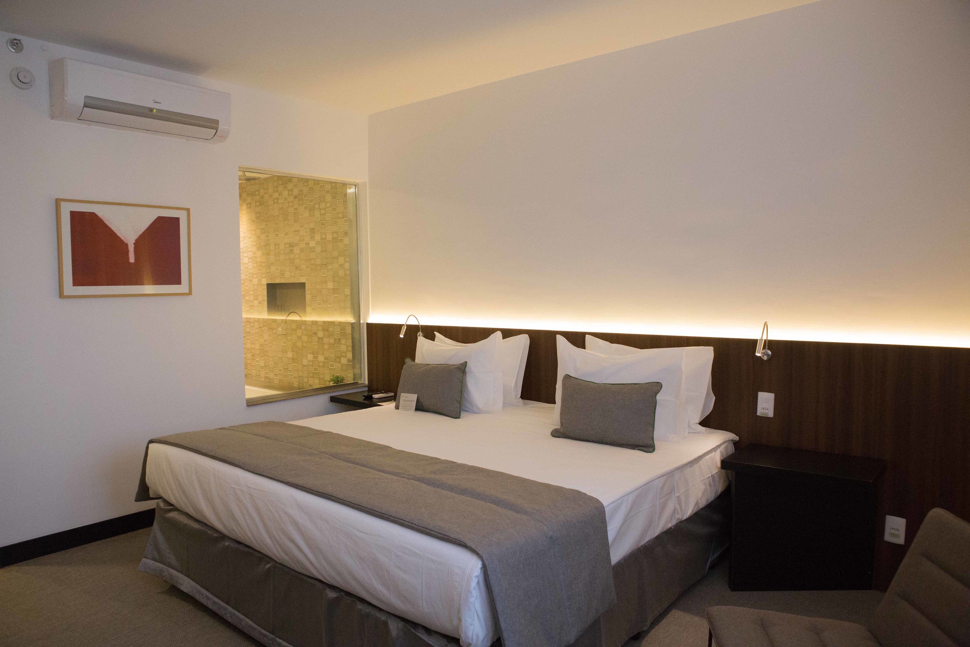 A hotel room with a bed, bedside tables, a mirror, and a wall-mounted air conditioner.