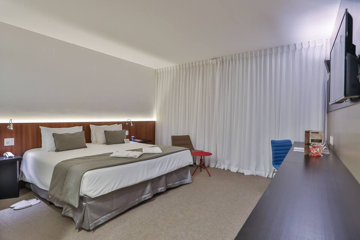 Habitación de hotel con una cama grande, un escritorio, una silla, una mesita y un televisor montado en la pared.