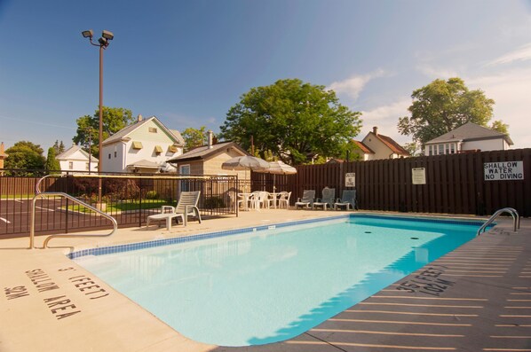 A swimming pool with a shallow water area, a wooden fence, and outdoor furniture.