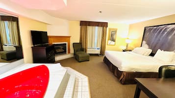 A hotel room with a bed, a desk, a chair, a TV, a fireplace, and a red bathtub.