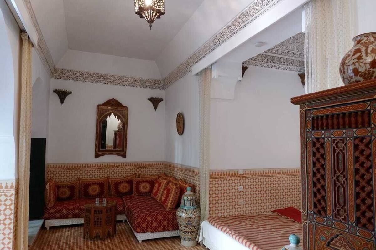 A room with a patterned floor, a sofa with cushions, a small table, a decorative vase, and a cabinet with intricate designs.