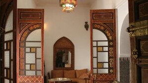A traditional interior with a patterned floor, a central seating area, and ornate wooden doors. - Riad Ifoulki (Marrakech)