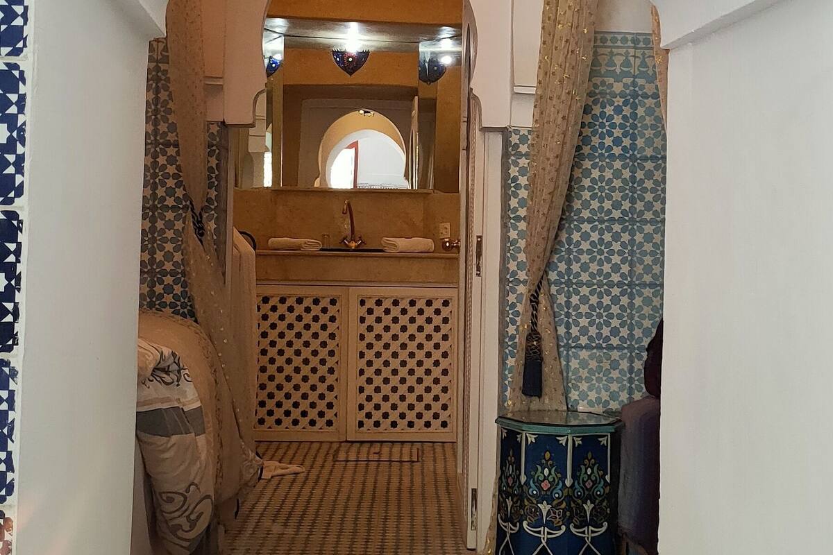A hallway with a patterned floor, a decorative archway, a hanging light fixture, and a small table with a blue and white patterned tablecloth.