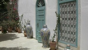 A courtyard with a white wall, two green doors, and several ornate vases. - Riad Ifoulki (Marrakech)
