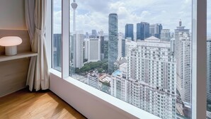 A room with a large window, a lamp, and a view of a cityscape with tall buildings and a tower. - Soho Suites KLCC by leala (Kuala Lumpur)