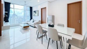 A modern hotel room with a large window, a sofa, a dining table with chairs, a refrigerator, and a door. - Soho Suites KLCC by leala (Kuala Lumpur)