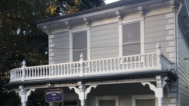 Un edificio de dos pisos con un balcón y un porche. Se ve un cartel que dice 'Broad Street Inn' y un buzón con la etiqueta 'Oficina'.