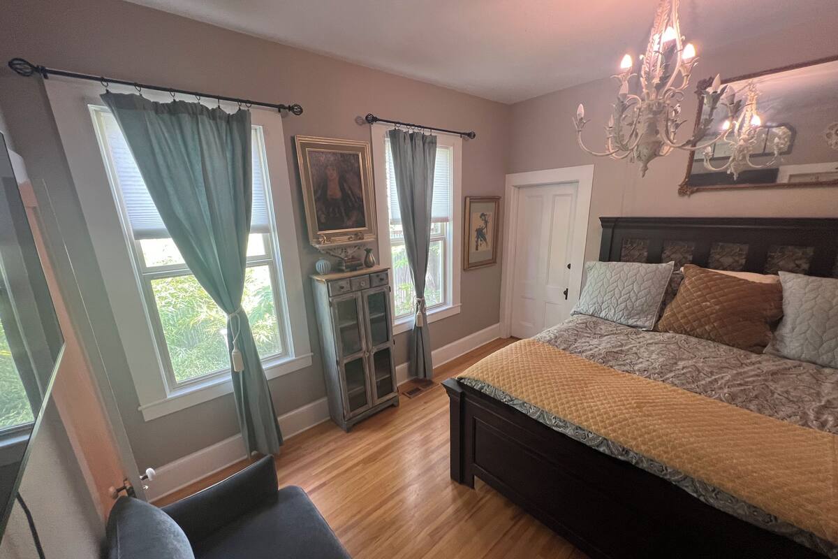 A bedroom with a large bed, a dresser, a chair, and a chandelier.