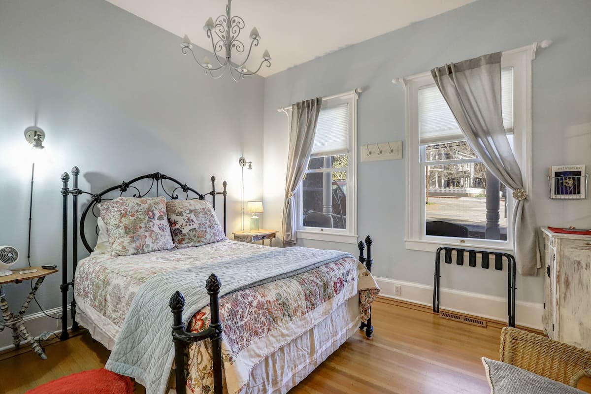 A bedroom with a bed, a nightstand, a lamp, a radiator, and a window with curtains.