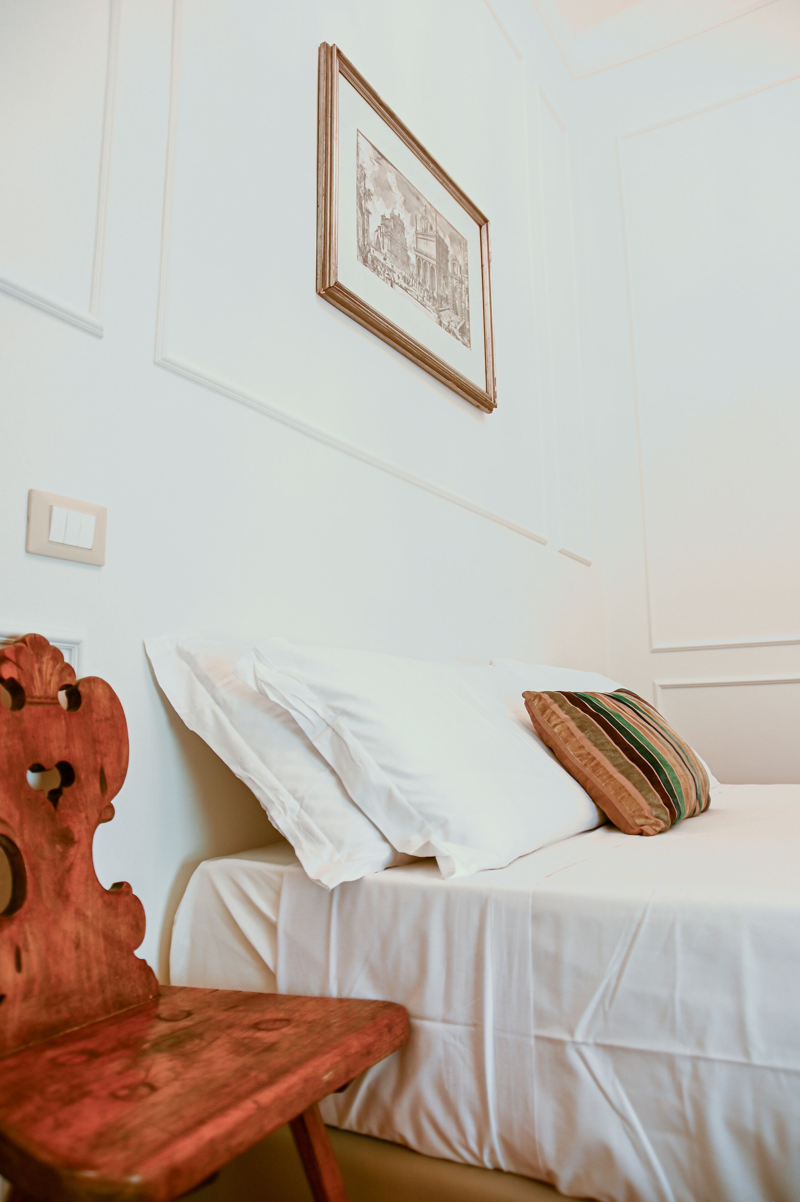 A bedroom with a bed, a wooden chair, and a framed picture on the wall.