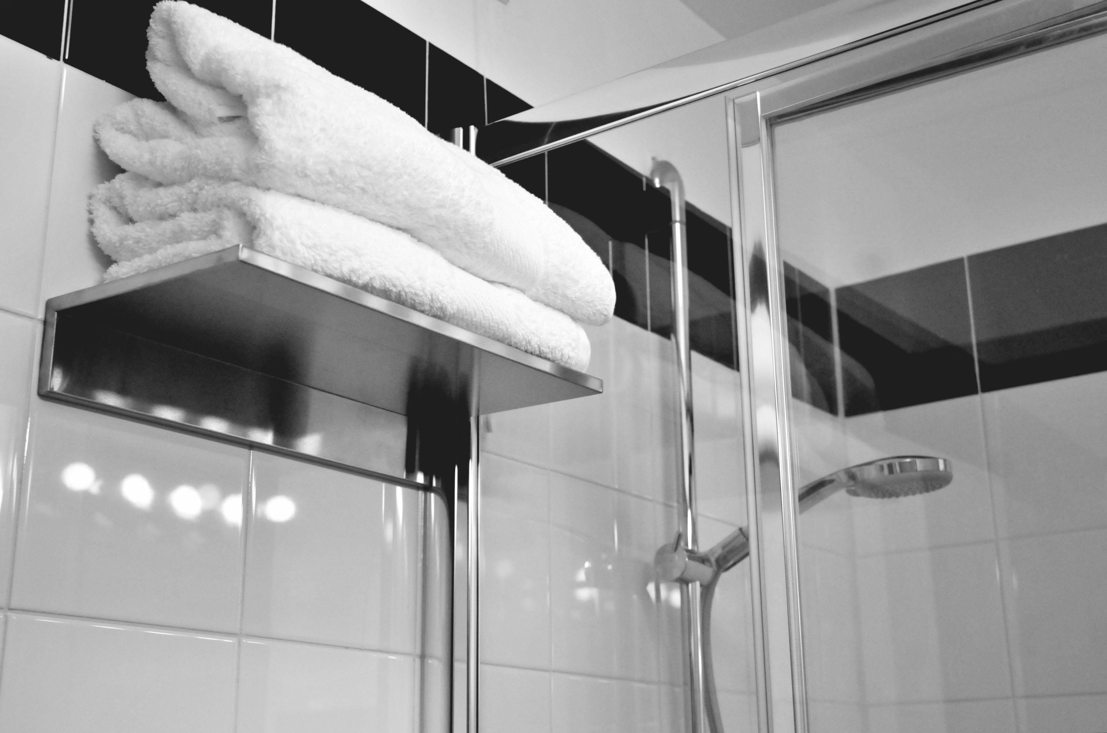 Un baño con cabina de ducha de vidrio, un perchero de metal y paredes con azulejos blancos.