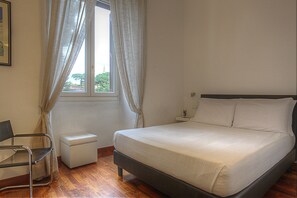 Un dormitorio con cama, una silla, una mesita de noche y una ventana con cortinas.