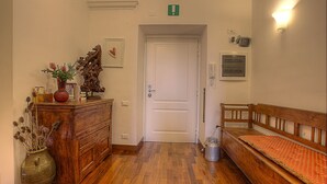 Un pasillo con un banco de madera, un jarrón con flores secas, un aparador de madera y una puerta blanca.