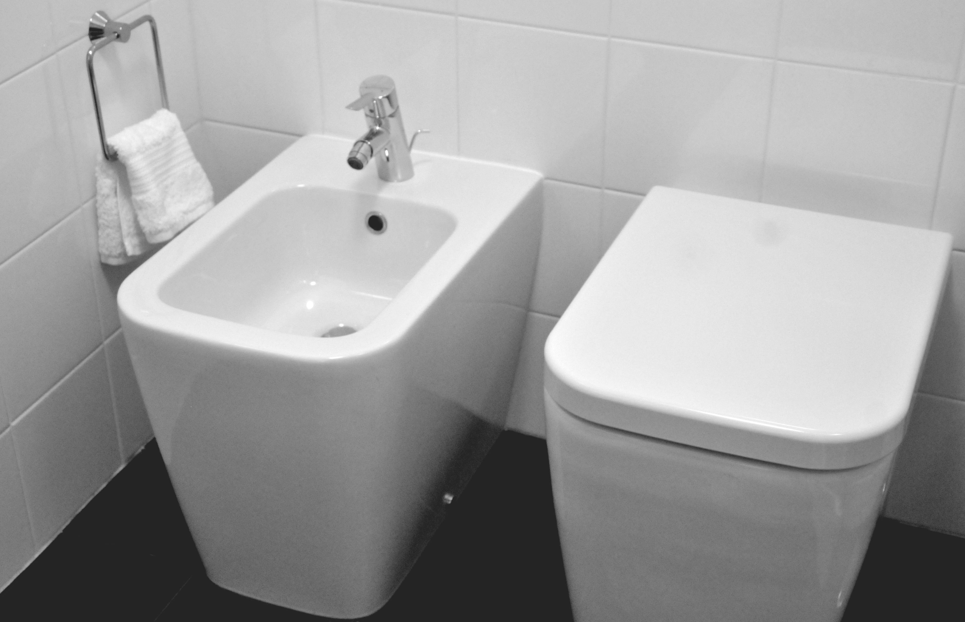 Un bagno con lavandino e WC bianchi, un porta asciugamani e pareti piastrellate.