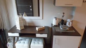 Cocina compacta con encimera oscura, refrigerador blanco y un pequeño comedor con dos taburetes blancos acolchados.