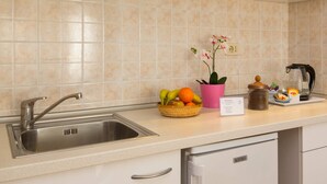 Una cocina con un lavamanos de acero inoxidable, una cesta de frutas, una orquídea en maceta, una cafetera y un cartel de bienvenida.