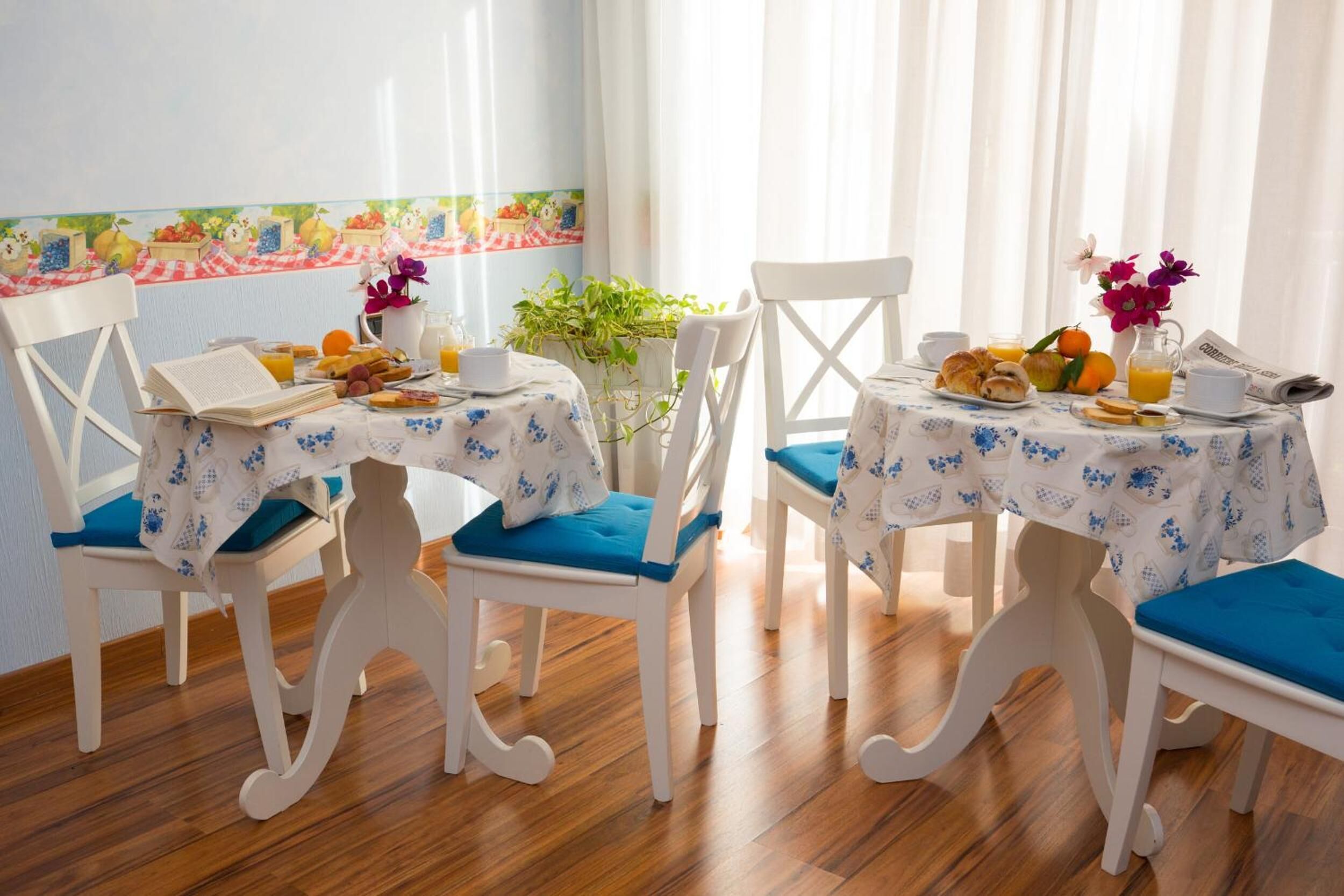 A breakfast setting with two white chairs, a table with a floral tablecloth, and a variety of breakfast items including croissants, oranges, and a pitcher of orange juice.