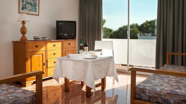 Een kamer met een eettafel, stoelen, een televisie, een kast en een balkon met uitzicht.