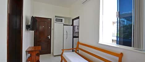 A compact living space with a wooden bench, a small table, a microwave, a refrigerator, and a ceiling fan.