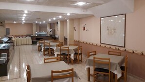 A dining area with multiple tables and chairs, a kitchen in the background, and a framed picture on the wall.