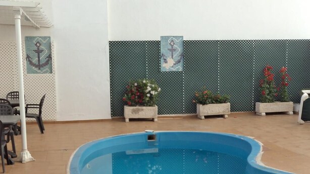 A swimming pool with tiled flooring, surrounded by potted plants and a white fence with a patterned design.