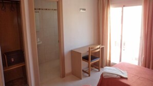 A hotel room with a bed, a desk, a wardrobe, and a sliding door leading to a bathroom.