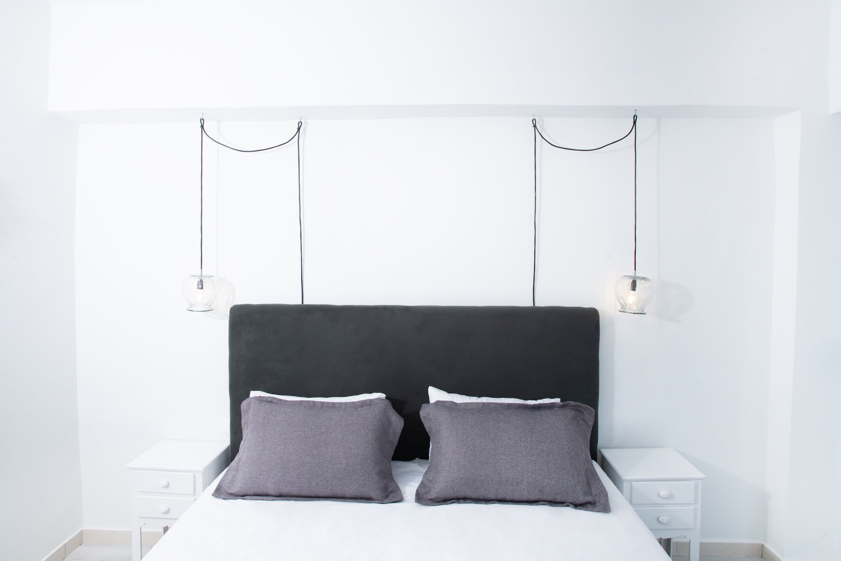 A modern bedroom with a black headboard, two bedside tables, and a white nightstand.