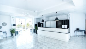 A modern reception area with a white reception desk, pendant lighting, and a view of the outside. - Bianco Olympico Beach Resort By Anayia AI Resorts (Polygyros)