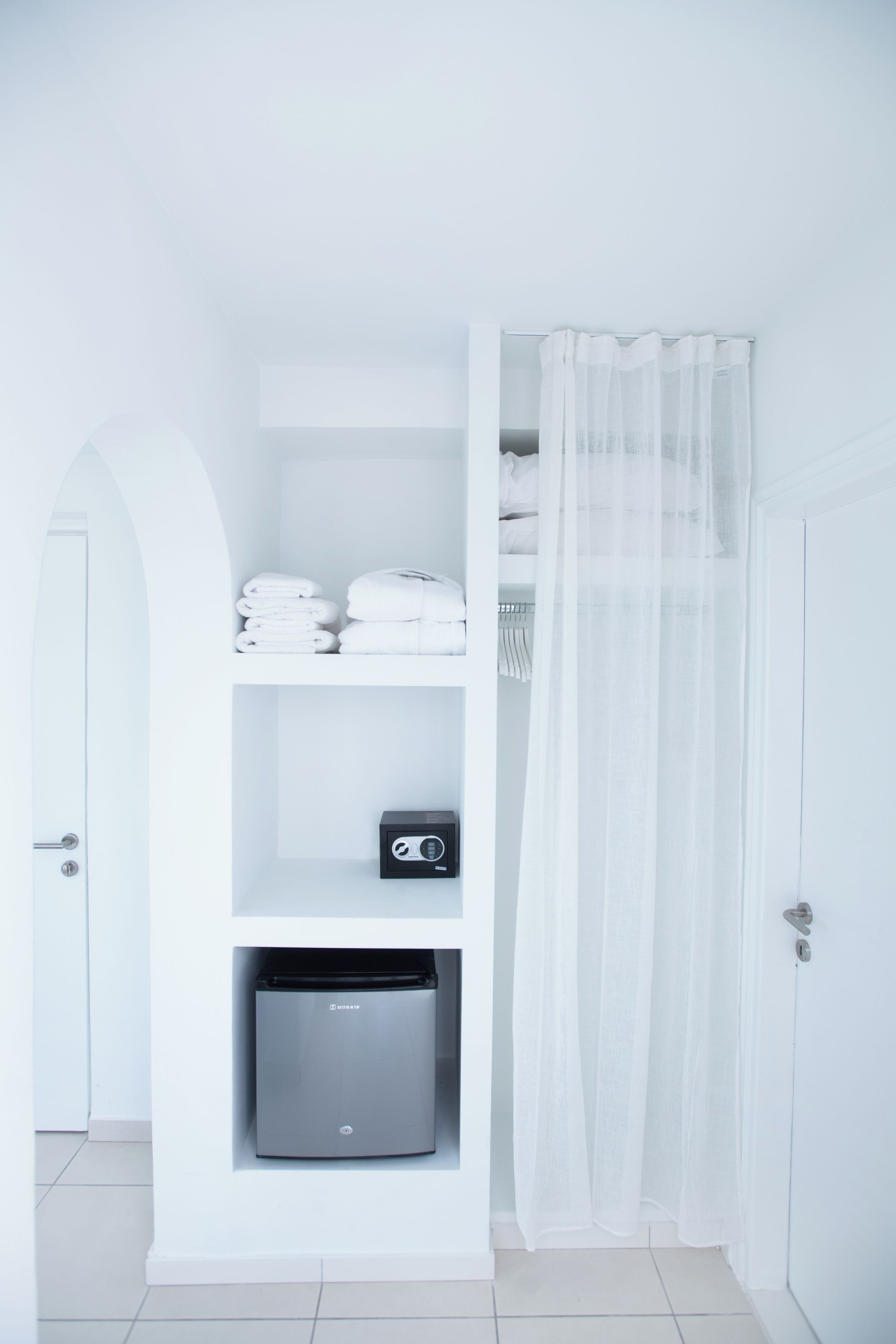 A white bathroom with a shower curtain, a towel rack, and a storage unit with a microwave.