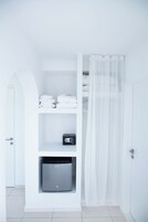 A white bathroom with a shower curtain, a towel rack, and a storage unit with a microwave.